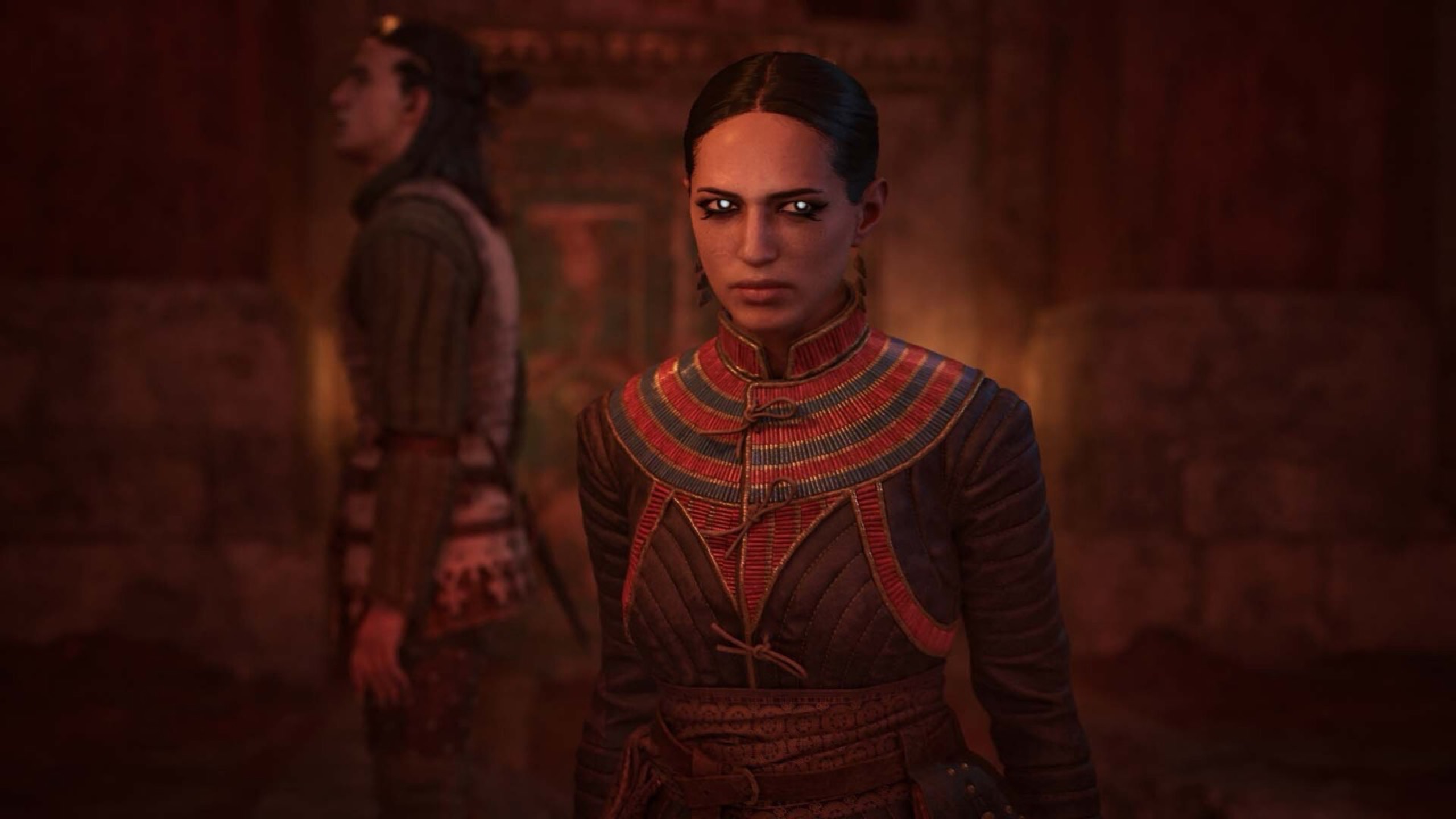 A woman in a red patterned tunic in a stone hall.